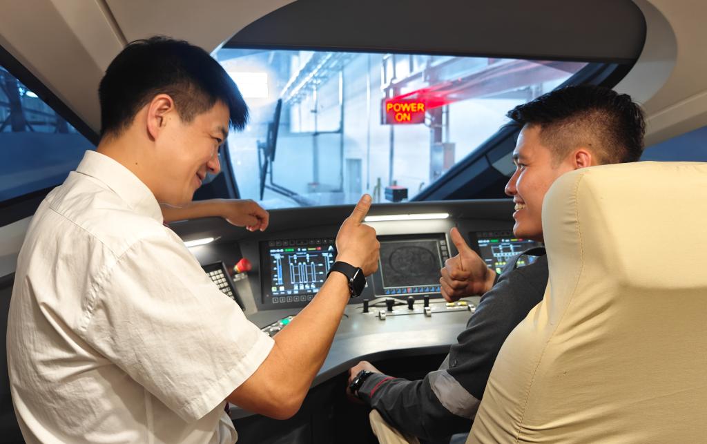 8月25日，在印度尼西亞萬隆的雅萬高鐵德卡魯爾動車所內(nèi)，中國師傅穆振（左）在向印尼火車司機塞蒂亞萬講解動車組出庫前的上電作業(yè)。