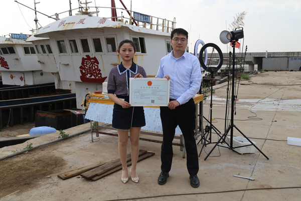 海鮮電商張夢琴與幫辦員手持食品經(jīng)營許可證合影。贛榆區(qū)委宣傳部供圖