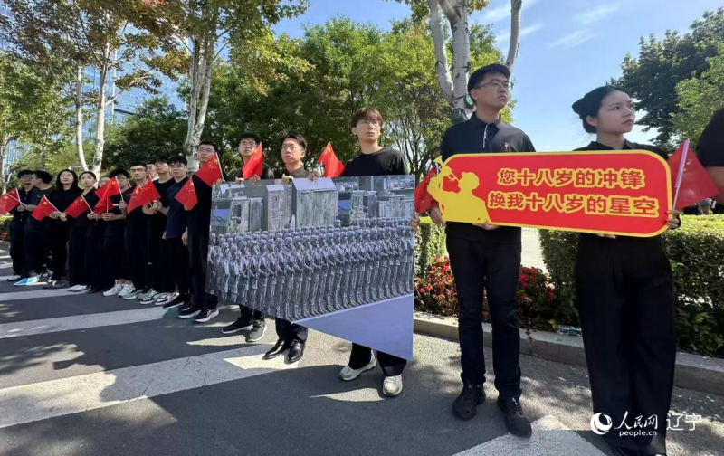 沈陽市人民廣場上，大學生們手持閱兵的圖片，告慰英烈。人民網(wǎng)記者 周頌雪攝
