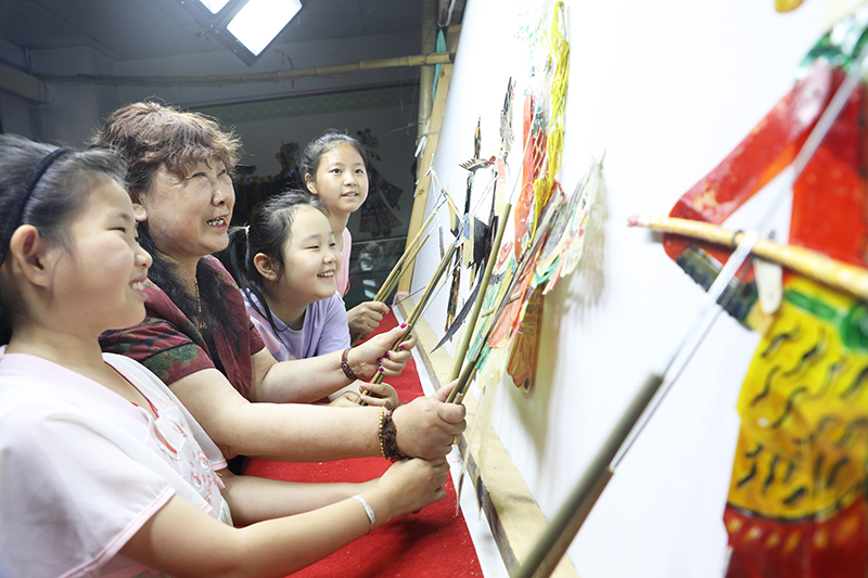 皮影藝人指導(dǎo)小朋友表演皮影戲。