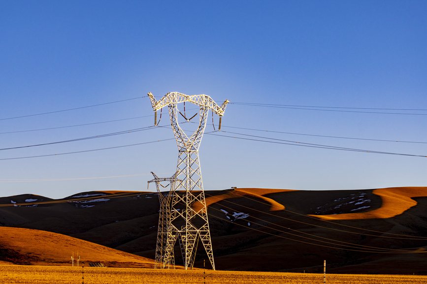 阿里地區(qū)的曠野上，電力鐵塔在夕陽下熠熠生輝。